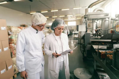 Dos profesionales revisan documentación de calidad y seguridad alimentaria en una planta de producción.
